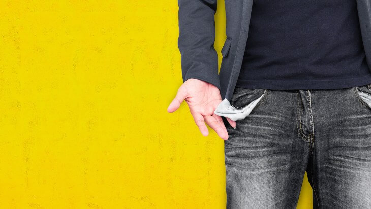 Man showing his empty pockets on yellow wall background.