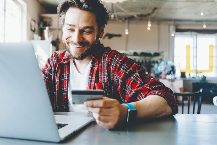 Portrait of man with stubble and flannel shirt. Smiling and shopping online with credit card