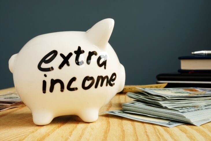 Extra income handwritten on a piggy bank and cash.