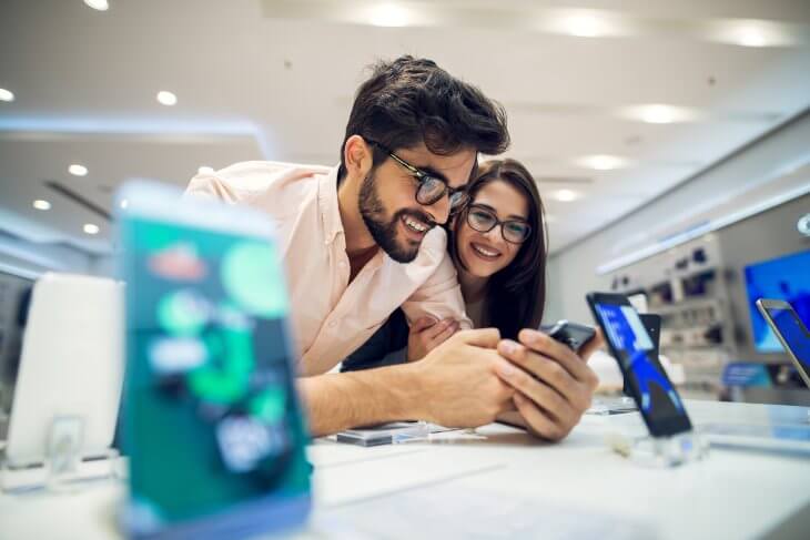 Close up focus view of a cheerful charming happy young student love couple choosing a new mobile in a tech store.